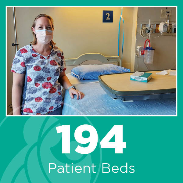 Image description: Team member in scrubs standing beside a patient bed in a patient room. White text on a green background reads: 194 Patient Beds. 
