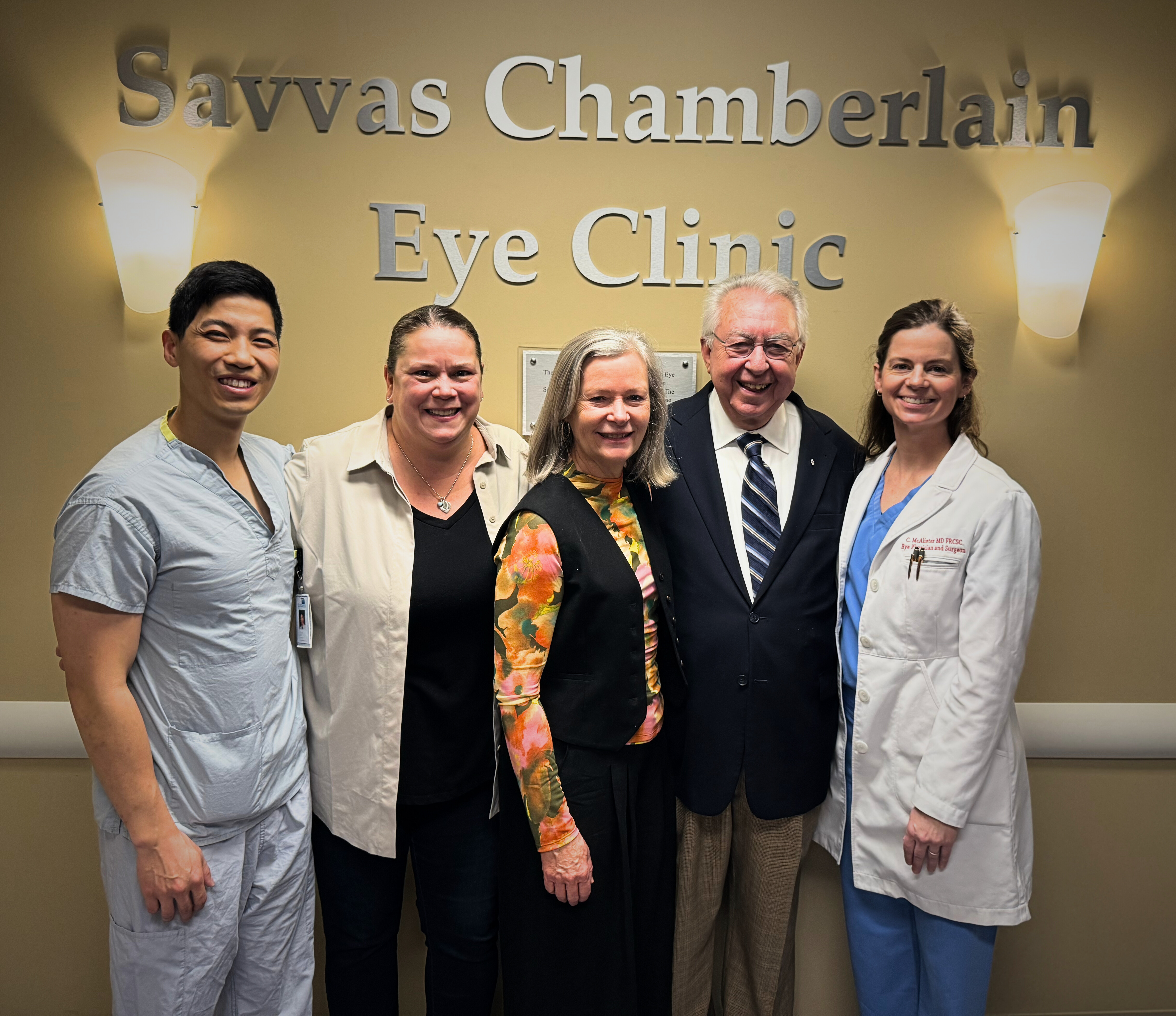 Group photo taken at the Retina Surgical Program and Eye Clinic donor naming. Left to right: Dr. Carl Shen, Maria Harper, Christine Chamberlain, Dr. Savvas Chamberlain, Dr. Chryssa McAlister stand together in front of the signage that reads: Savvas Chamberlain Eye Clinic